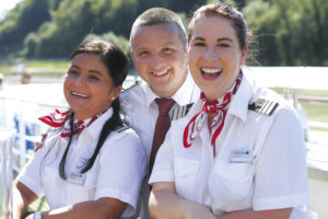 Lächelnde Crewmitglieder in Uniform mit Halstüchern, die Freude und Gastfreundschaft am Schiffsausflug zeigen.