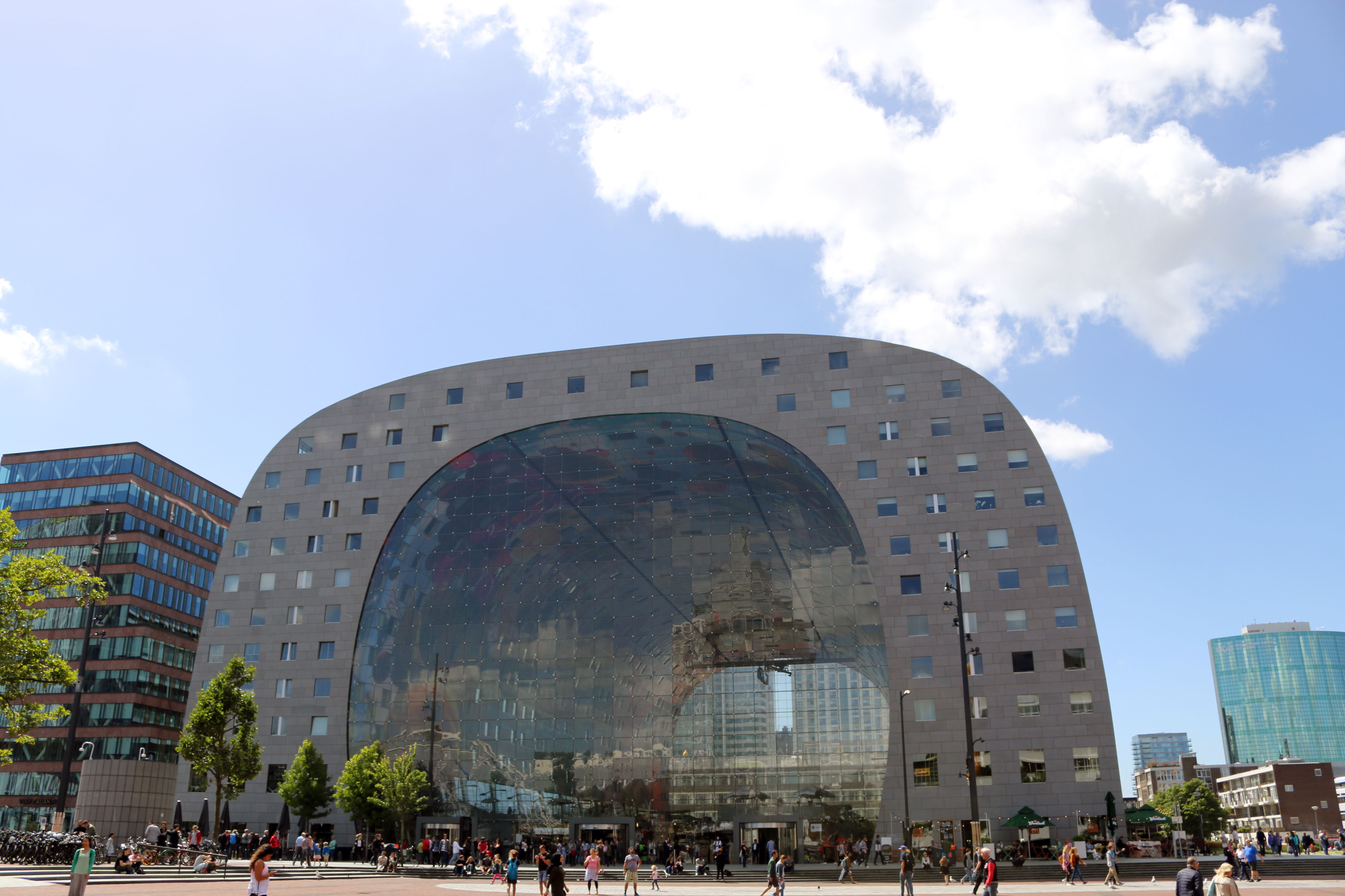 Die Markthalle Rotterdam an einem sonnigen Mittag mit blauem Himmel, Glasfassade spiegelt die Skyline und lockt viele Besucher an.