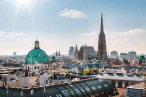 Am Vormittag liegt die Wiener Innenstadt mit Karlskirche und Stephansdom unter klarem Himmel und sonnigem Licht.