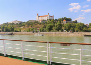 Bratislavaer Burg auf einem bewaldeten Hügel über der Donau, gesehen von einem Schiff mit weißem Geländer
