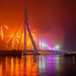 Erasmusbrücke in Rotterdam bei Nacht mit buntem Feuerwerk und Reflexionen im Wasser
