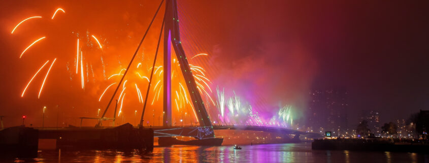 Erasmusbrücke in Rotterdam bei Nacht mit buntem Feuerwerk und Reflexionen im Wasser