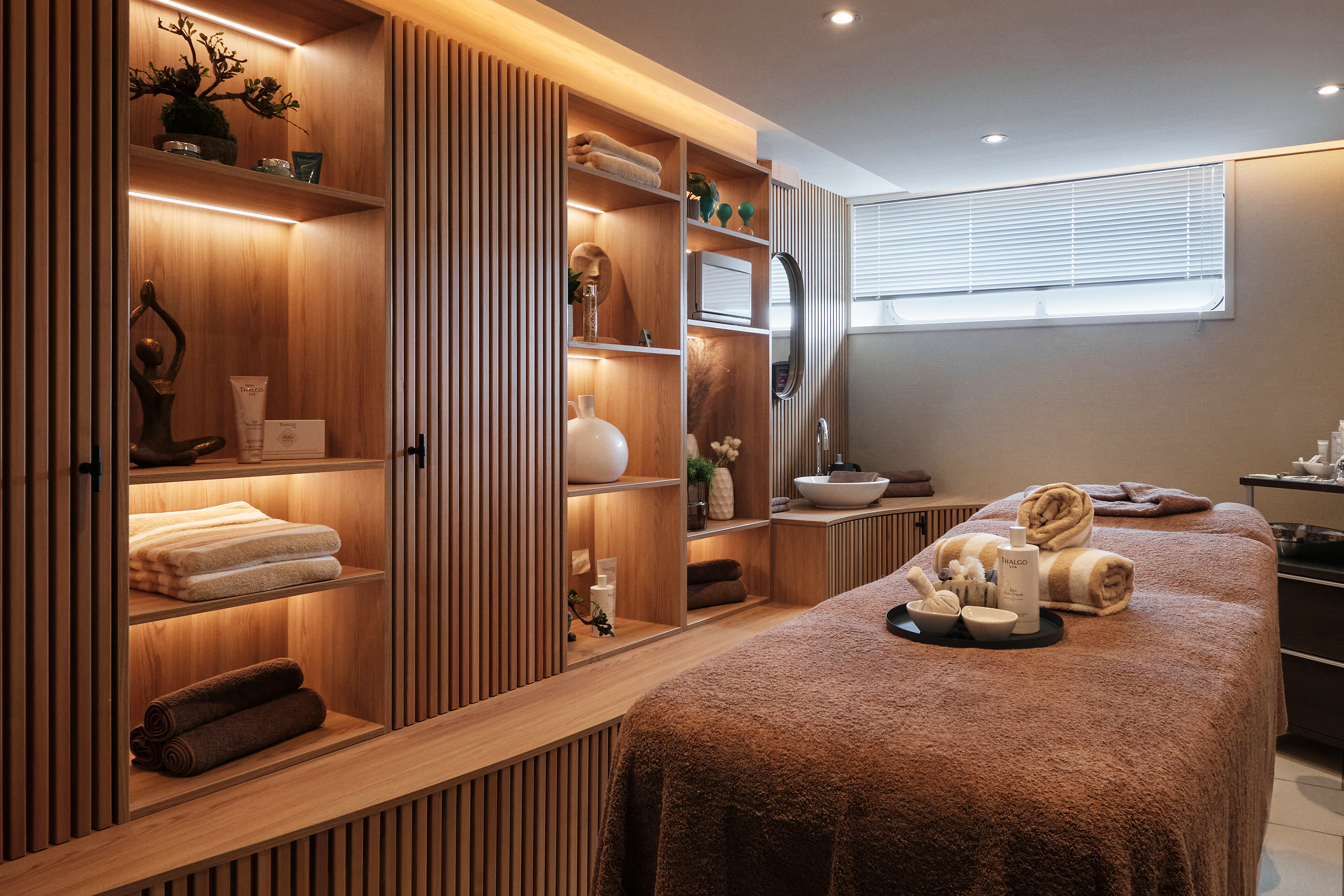Stilvoller Behandlungsraum im SPA mit warmem Licht, Holzregalen, Massageliege und dekorativen Wellness-Accessoires.