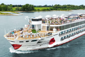 Die A-ROSA SENA fährt über den Fluss, während Gäste auf dem Sonnendeck unter weißen Schirmen entspannen.