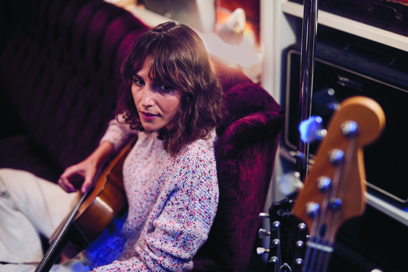 Eine Frau spielt Gitarre auf einer Couch, umgeben von Gitarren und Lautsprechern.
