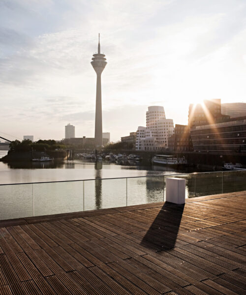 Medienhafen Düsseldorf Die Sonne geht am frühen Abend hinter dem Rheinturm im Düsseldorfer MedienHafen unter und wirft lange Schatten auf die hölzerne Promenade.