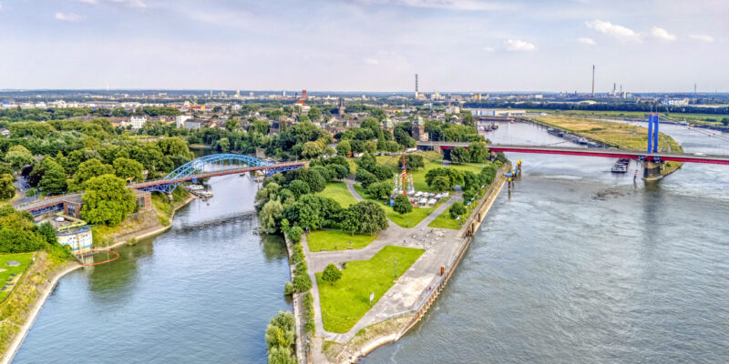 Luftaufnahme der Mercatorinsel an der Mühlenweide in Duisburg am Rhein. Wege und Grünflächen liegen zwischen Hafenbecken und Fluss, Brücken verbinden die Ufer.